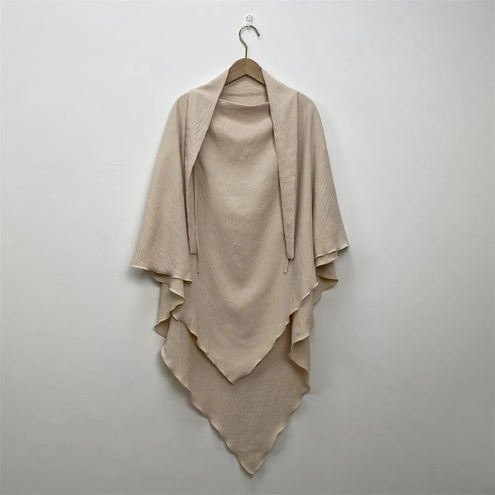 A beige two-layer everyday hijab scarf draped on a hanger against a light gray wall.