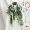 Bufanda estampada floral verde y azul drapeada sobre una camisa blanca, exhibida en percha.