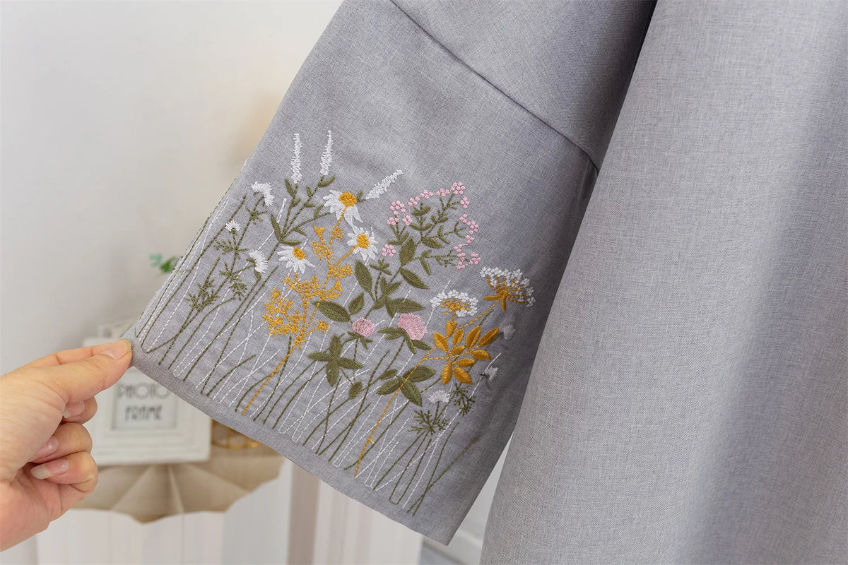 Nahaufnahme einer grauen Abayasärmel mit zarten floralen Stickereien in weißem, gelbem und rosa Faden.