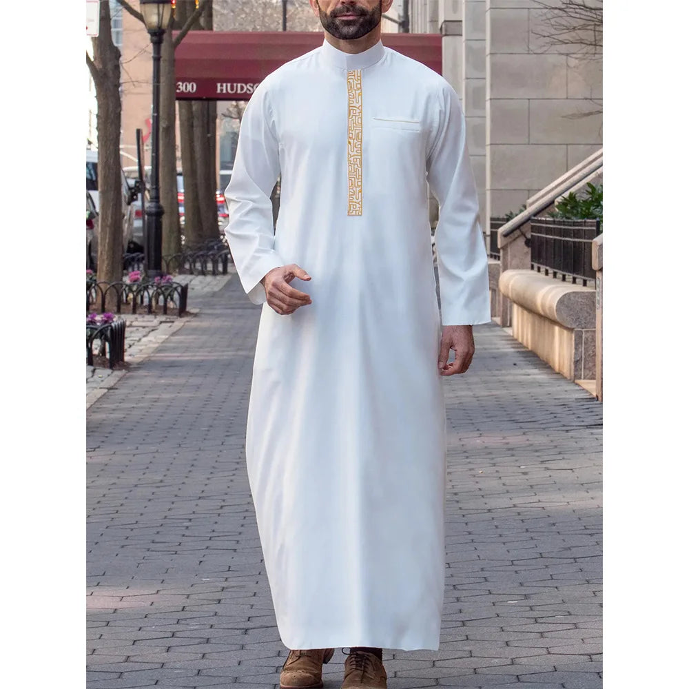 Un homme portant une robe musulmane blanche à col verticaux dorés marche sur un trottoir.