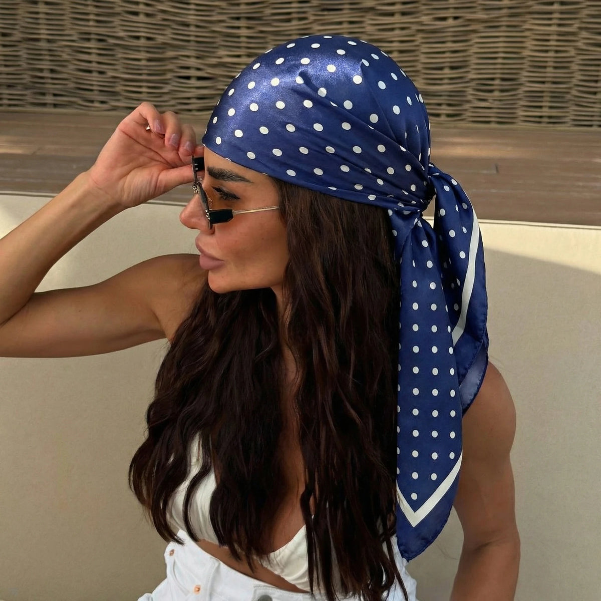 A woman wearing a blue polka dot silk scarf tied around her head and hair.