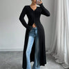 Eine Frau modelliert einen schwarzen, gerippten Strick-Maxirober über blauen Jeans, posiert drinnen.