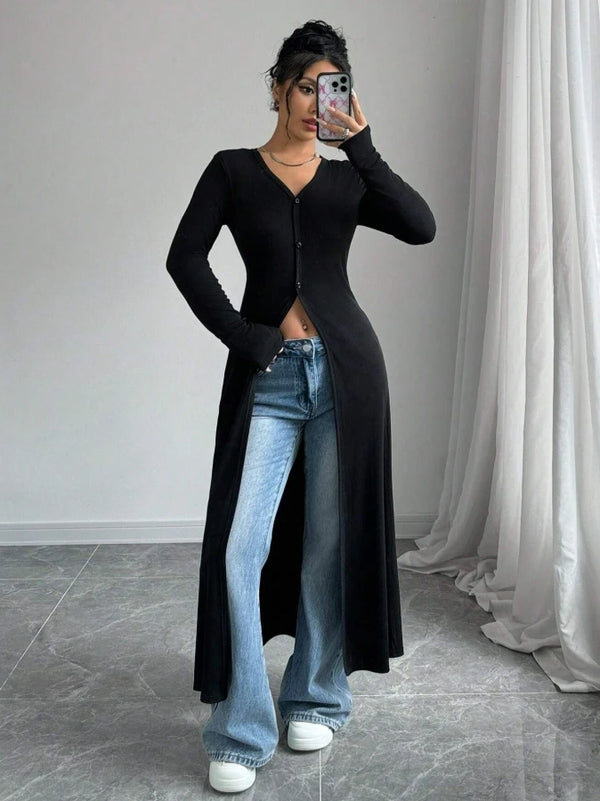 A woman models a black ribbed knit maxi cardigan over blue jeans, posing indoors.