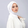Eine Frau mit weißem Instant-Turban-Hijab, Untercap-Bonnet und weißem Oberteil blickt direkt in die Kamera.