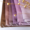 Stapel von Crinkle-Satin-Chiffon-Hijabs in Mauve-, Violett- und Lilatönen mit goldenen floralen Akzenten.