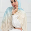 Una mujer vistiendo un pañuelo hijab de algodón gradiente de doble cara en tonos azul claro y crema.