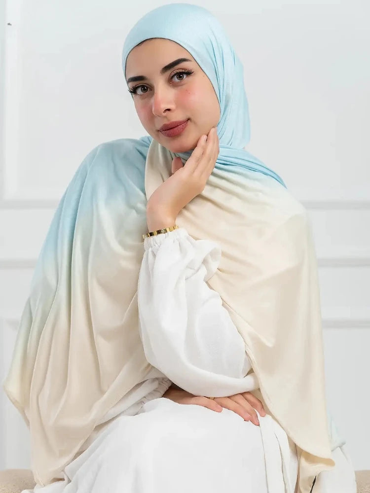 Una mujer vistiendo un pañuelo hijab de algodón gradiente de doble cara en tonos azul claro y crema.