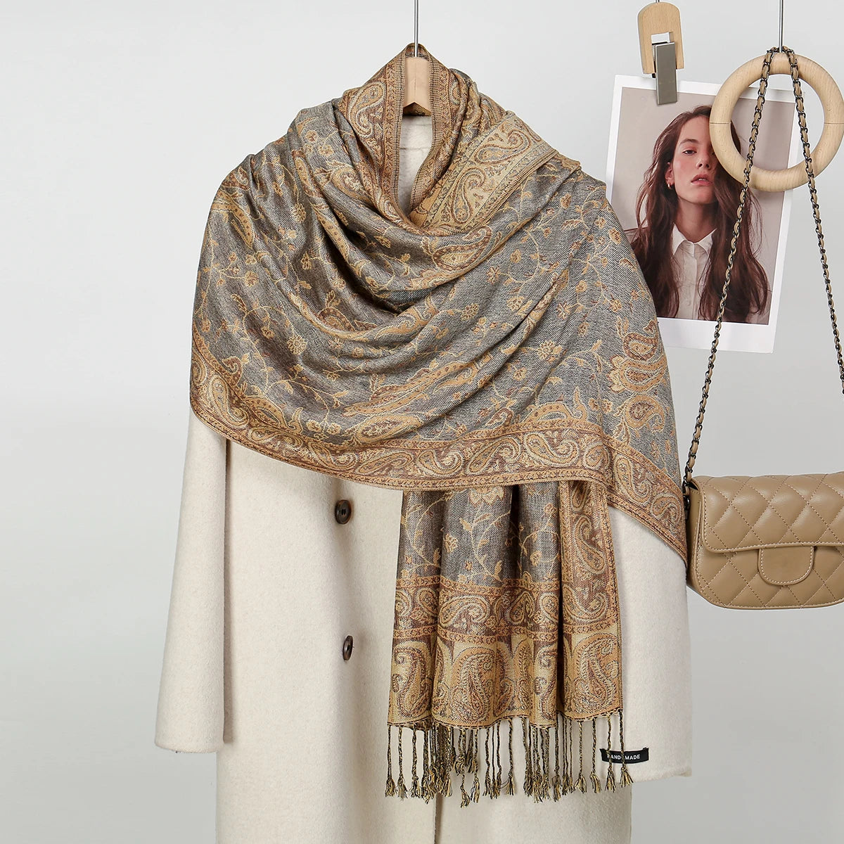 Un suéter de punto beige muestra un chal bordado con estampado paisley marrón y dorado colgado alrededor del cuello.