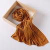 A golden brown ribbed jersey hijab scarf is displayed within a light wooden frame.