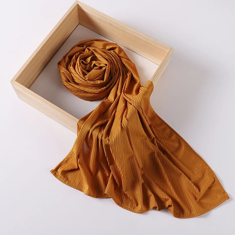 A golden brown ribbed jersey hijab scarf is displayed within a light wooden frame.