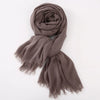 Un foulard hijab en coton viscose taupe avec franges et pompon, roulé en spirale.