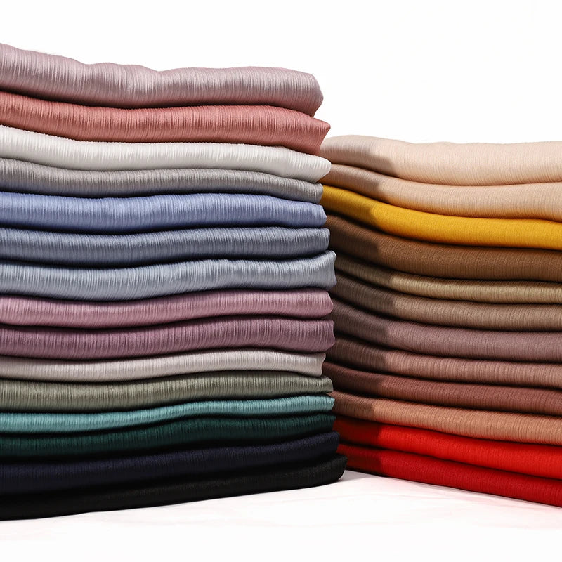 Gestapelte, gefaltete Premium-Satin-Hijabs in verschiedenen gedämpften und erdigen Tönen.