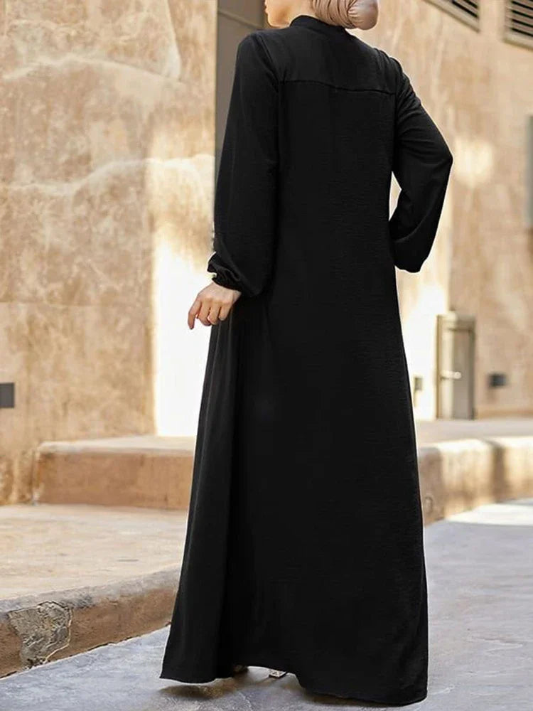 Une femme portant une élégante robe longue noire ample à col montant, vue de dos.