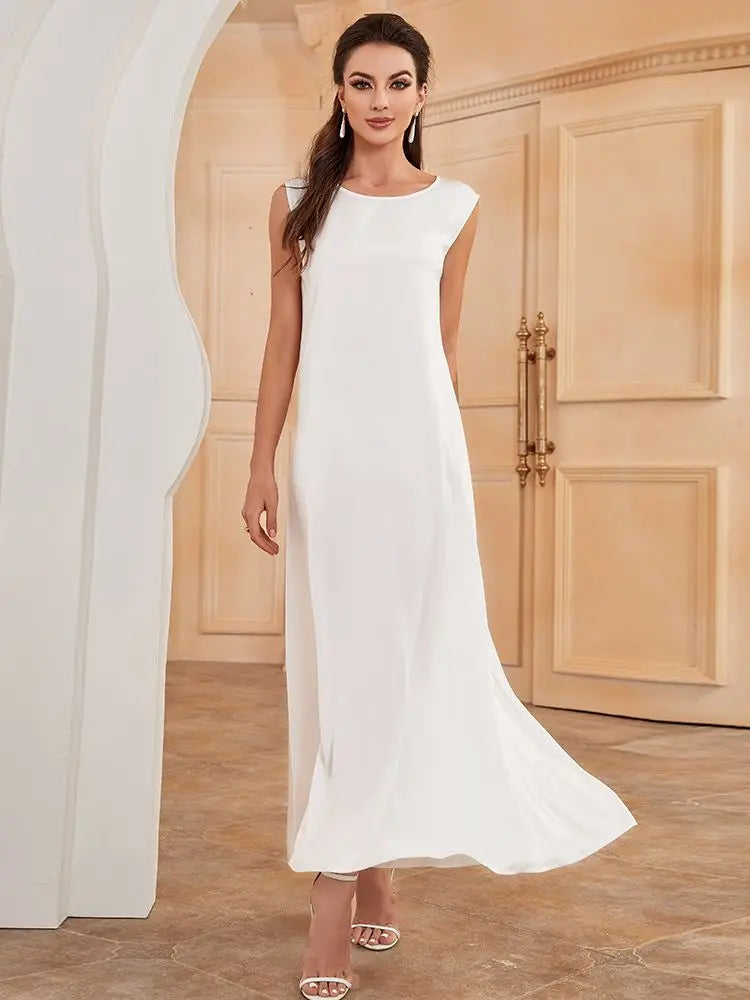 A woman models a white flowing modest abaya dress in a light beige room.