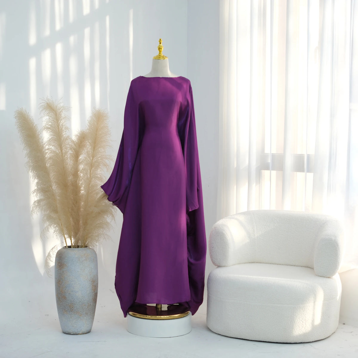 Lila eleganter Kaftan-Kleid auf einem Mannequin neben einem weißen Sessel am Fenster.