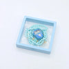 A blue wooden box holds a string of light blue prayer beads and a digital counter bracelet.