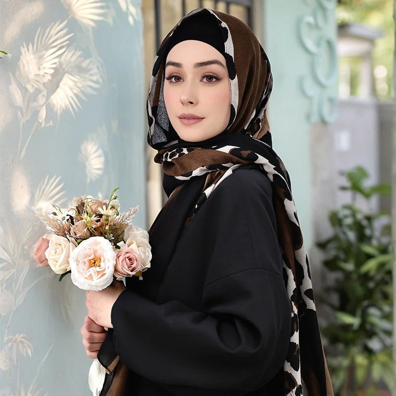 Une femme portant une tenue noire et un hijab en viscose à imprimé léopard, tenant un bouquet de fleurs.