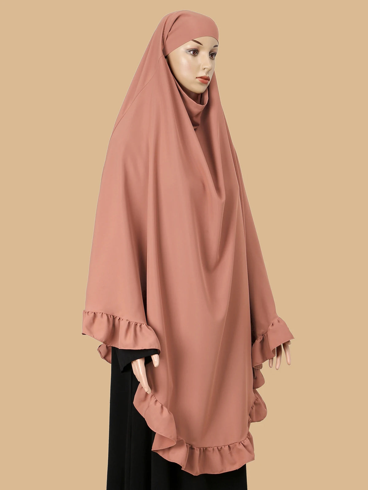 Eine Frau trägt einen staubrosa Strass-Hijabschal, der über ihren Kopf und ihre Schultern drapiert ist.