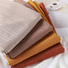 A stack of ribbed jersey hijab scarves in various earth tones including beige, brown, gold, and rust.