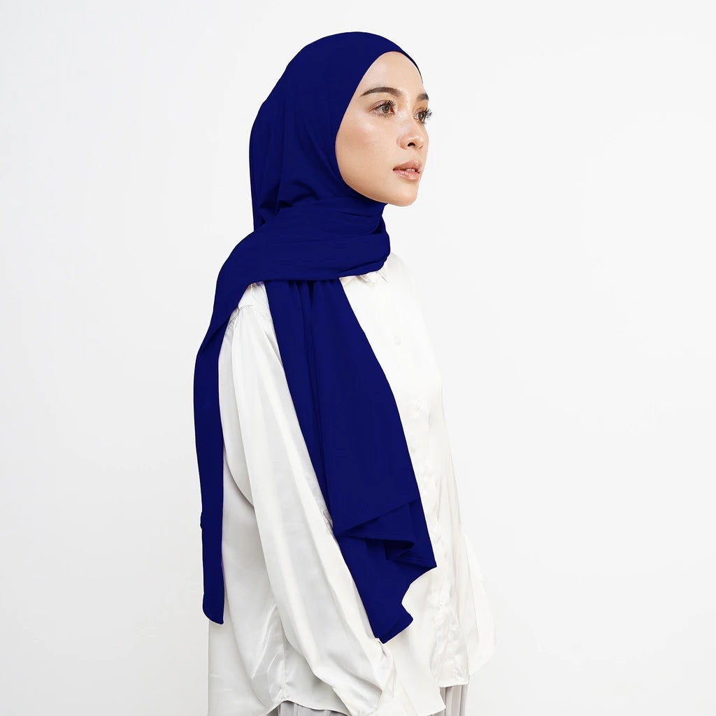 Eine Frau trägt einen königsblauen weichen Baumwolljersey-Instant-Hijab-Schal über einem weißen Top.