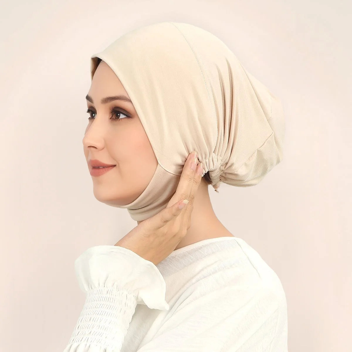 Une femme portant un hijab uni beige et un haut blanc, regardant sur le côté.