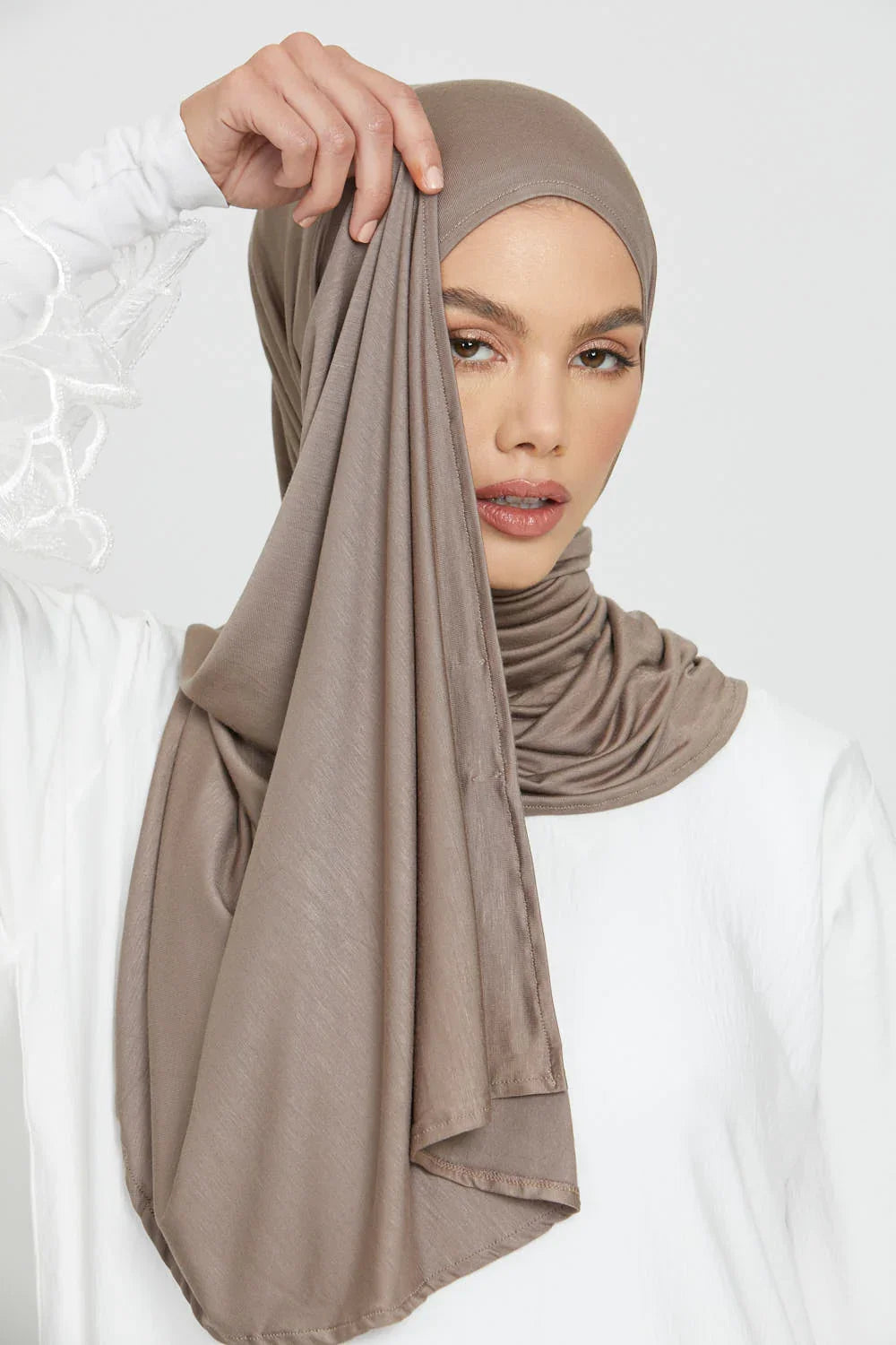 Eine Frau trägt einen einfarbigen taupefarbenen Jersey-Hijab, der über ihren Kopf und Hals drapiert ist.