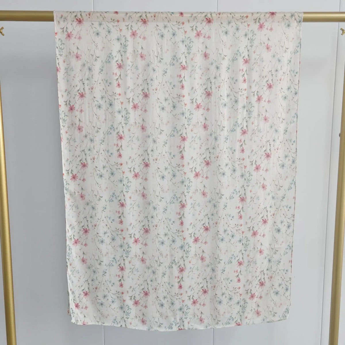Durchsichtiger weißer Schal mit zarter Blumenmuster in rosa und blauen Blüten, aufgehängt an einem goldenen Haken.