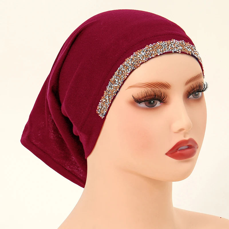Una modelo lleva un hiyab interior de algodón modal elástico color borgoña intenso con un ribete dorado brillante.