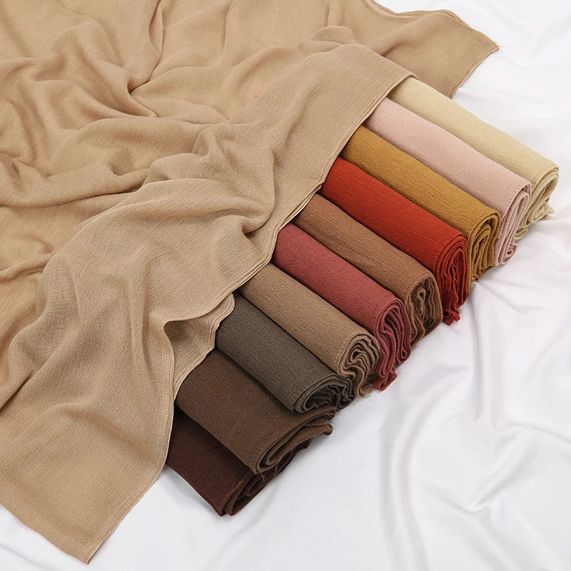 Pile de foulards ou châles en crêpe rayonnée aux tons terreux : beige, terre cuite et vert olive.