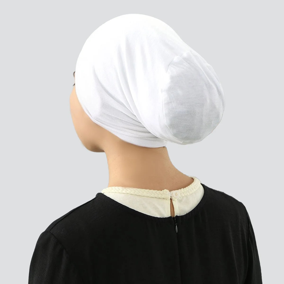 Una mujer vistiendo una gorra interior de hijab blanca elástica y una blusa negra.