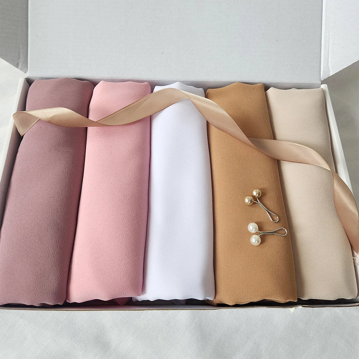 Una caja con un juego de cinco pañuelos de chifón para hijab de colores sólidos en tonos rosa, beige y crema.
