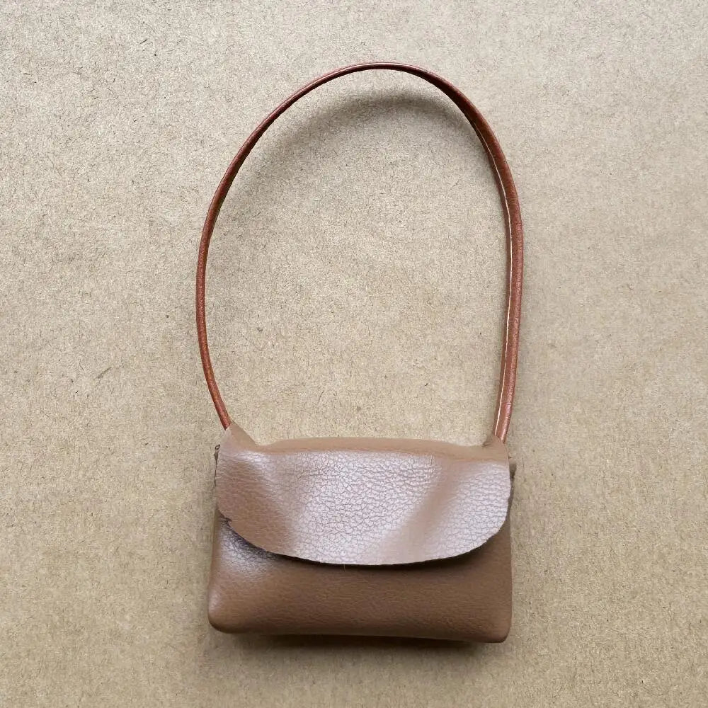 Un pequeño bolso cruz de cuero marrón claro con una correa delgada de cuero marrón sobre un fondo neutro.