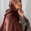A woman wearing a solid terracotta brown soft modal rayon hijab set with a gray sweater.