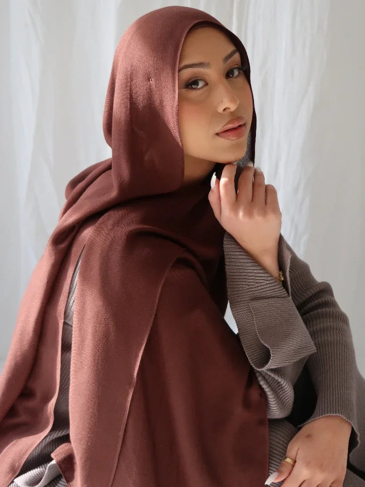 A woman wearing a solid terracotta brown soft modal rayon hijab set with a gray sweater.