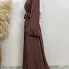 Eine Frau trägt einen fließenden, offengebundenen Abaya-Kaftan in dunkelbrauner Farbe mit weißen Akzenten.