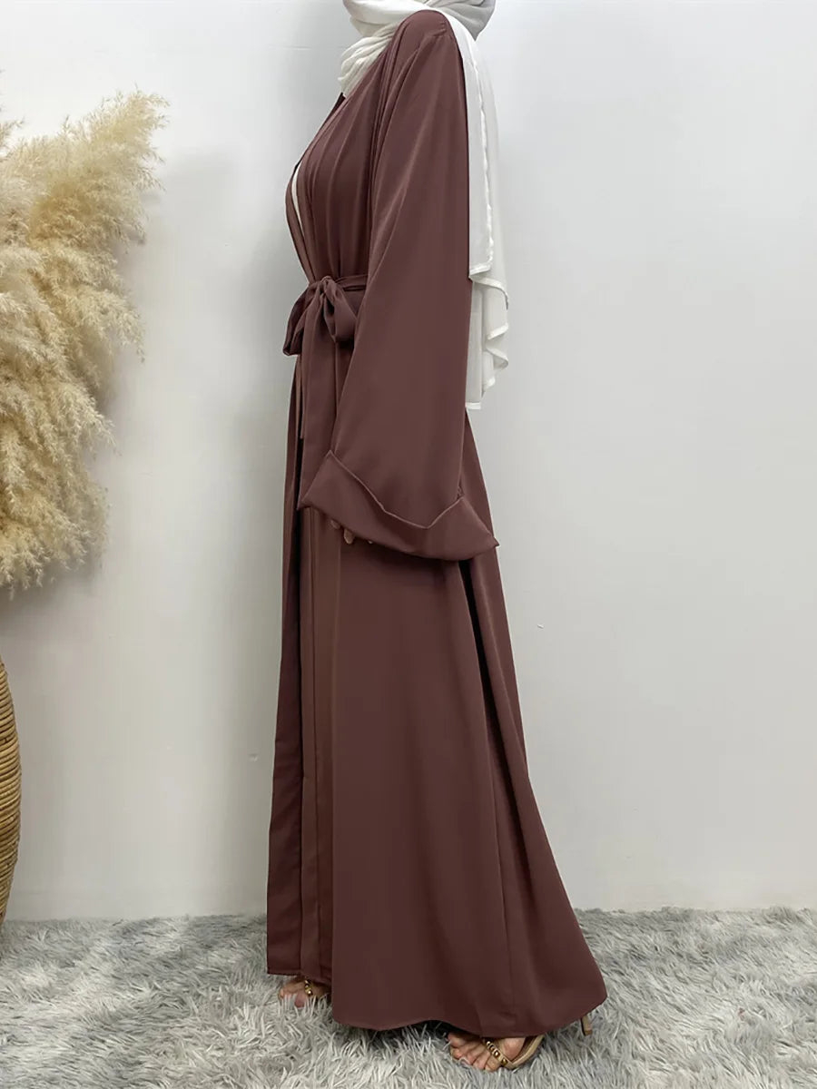 Eine Frau trägt einen fließenden, offengebundenen Abaya-Kaftan in dunkelbrauner Farbe mit weißen Akzenten.