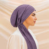 A woman wearing a purple solid color turban hijab cap and white clothing, shown in profile.