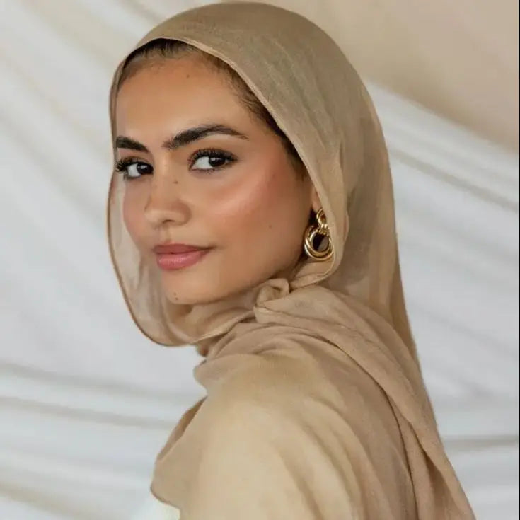 Eine Frau trägt einen eleganten, einfachen beige Viskose-Hijab und blickt direkt in die Kamera.