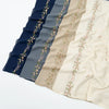 A display of elegant floral embroidery chiffon hijabs or shawls in various shades of blue, gray, and cream.