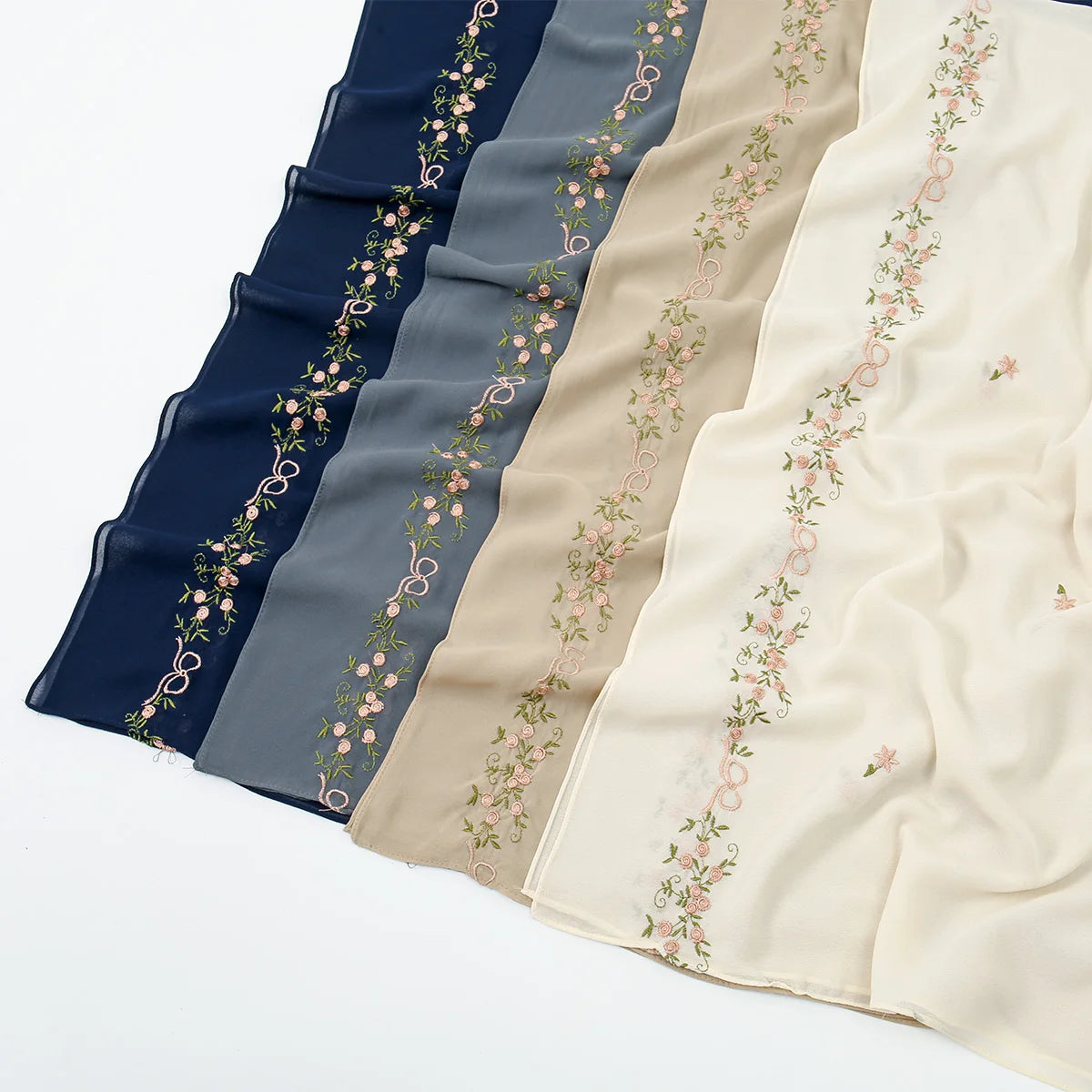A display of elegant floral embroidery chiffon hijabs or shawls in various shades of blue, gray, and cream.