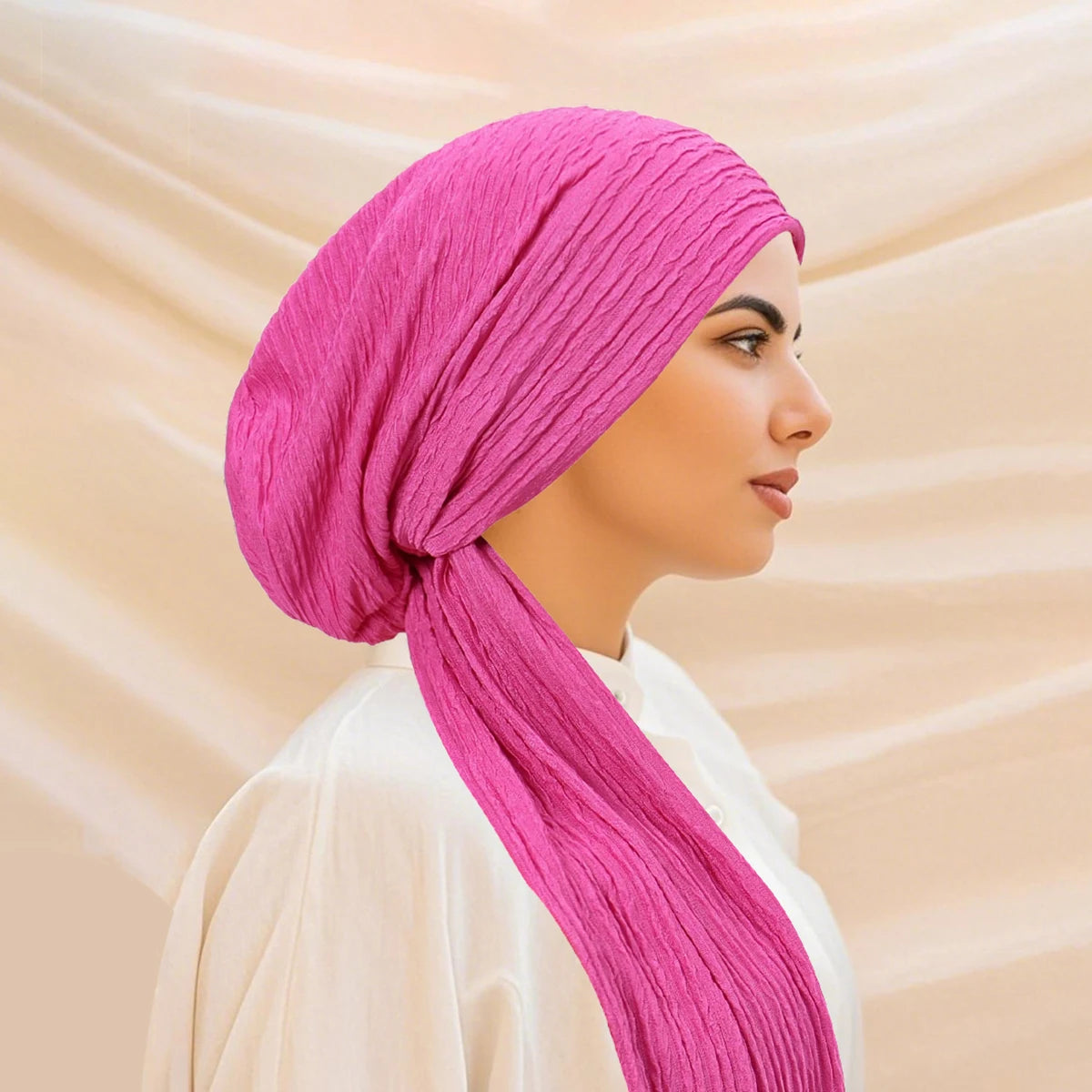 A woman wearing a vibrant pink solid color turban hijab cap and white clothing.
