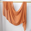 Écharpe hijab orange fluide et solide drapée sur un cintre en bois sur fond blanc.