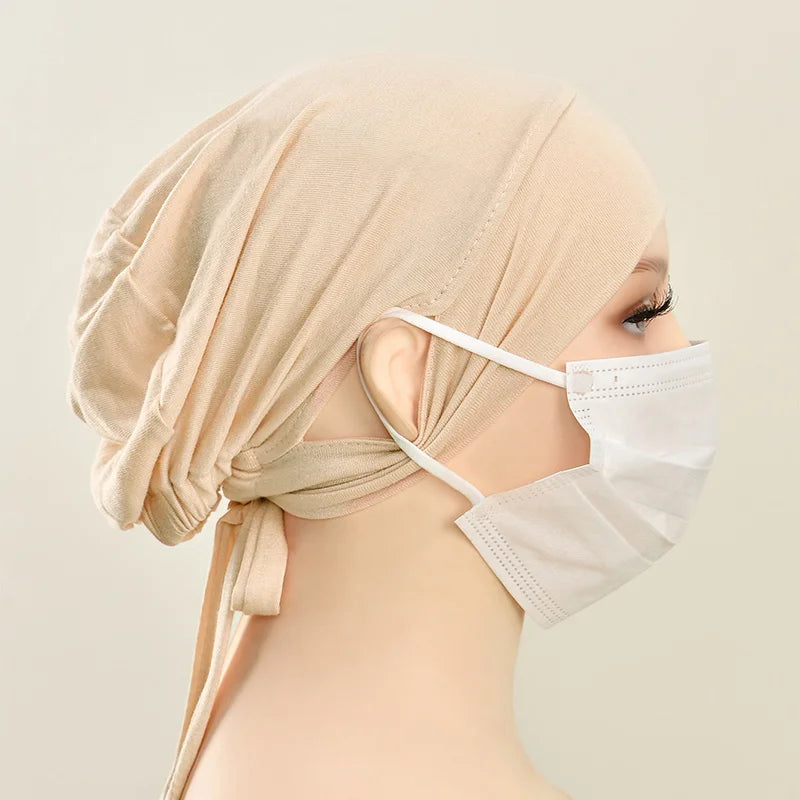 Eine Frau trägt eine beige Jersey-Baumwoll-Hijabkappe und eine weiße Schutzmaske.