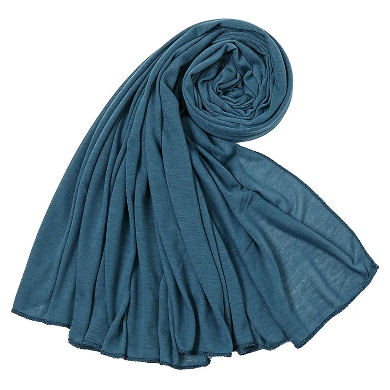 Un foulard hijab en jersey de coton bleu sarcelle roulé et drapé, montrant sa texture douce.