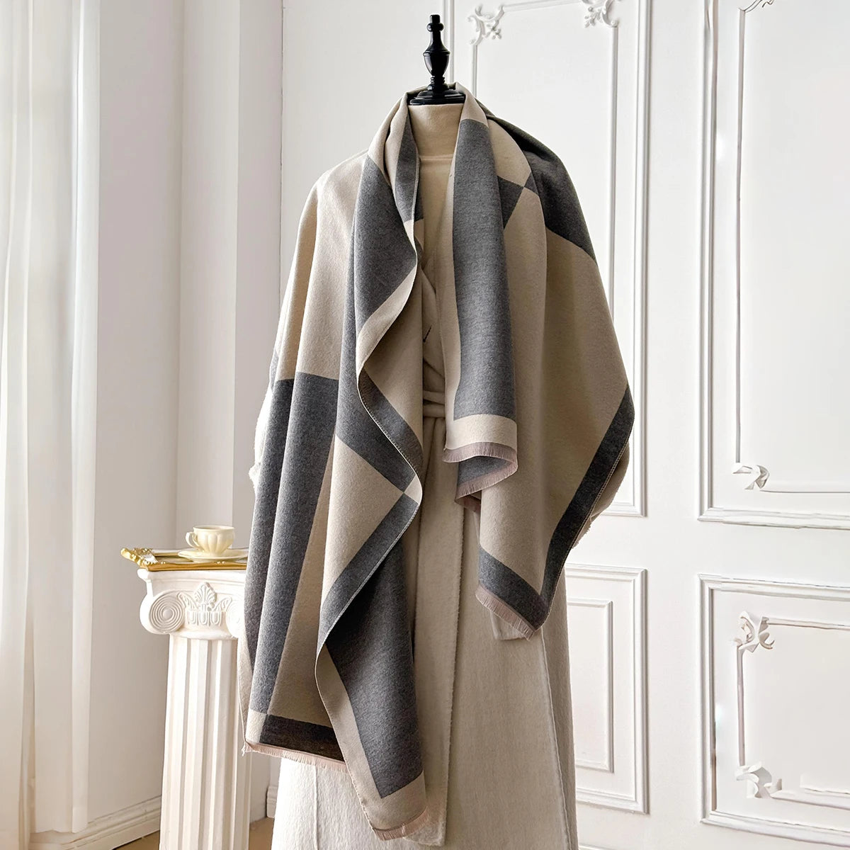 Pañuelo pashmina geométrico beige y gris drapeado sobre un perchero contra una pared blanca.