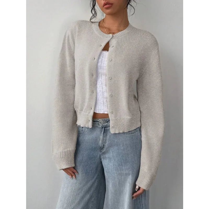 Une femme portant un pull tricoté beige clair sur un haut blanc et un jean bleu.