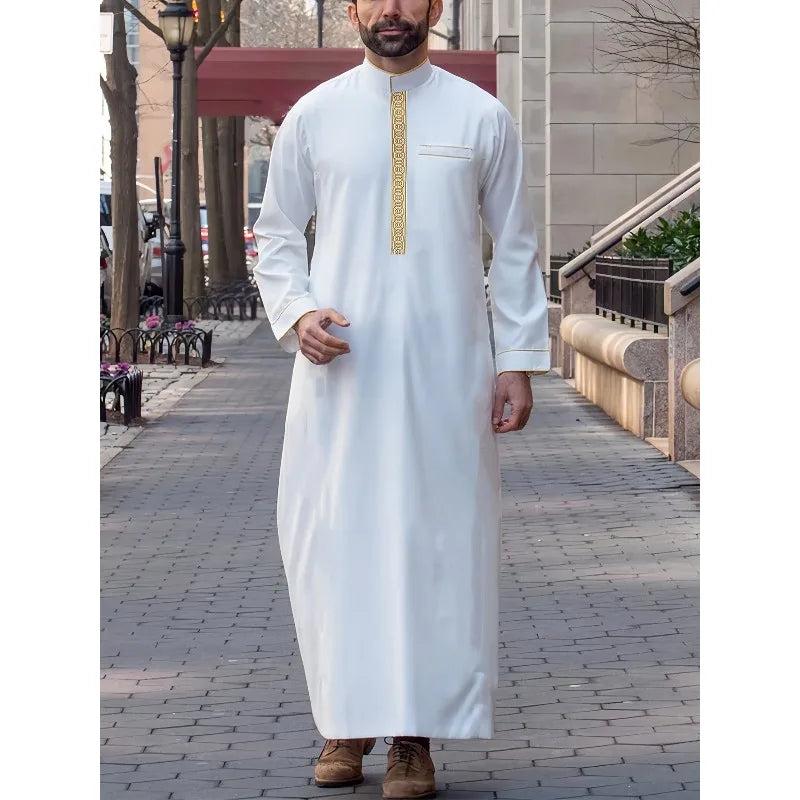 A man wearing a white embroidered long-sleeve thobe or jubbah in an outdoor setting.