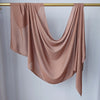 Un foulard modal rose fluide et solide drapé sur un cintre en bois.