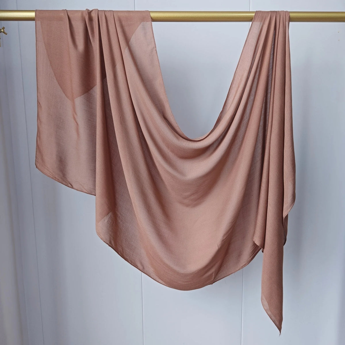 Un foulard modal rose fluide et solide drapé sur un cintre en bois.
