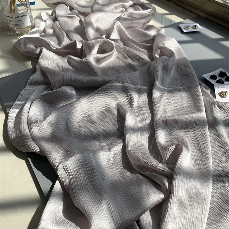 Ein drapiertes hellgraues Crinkle-Satin-Chiffon-Hijabgewebe in weichen Falten auf einer Oberfläche.